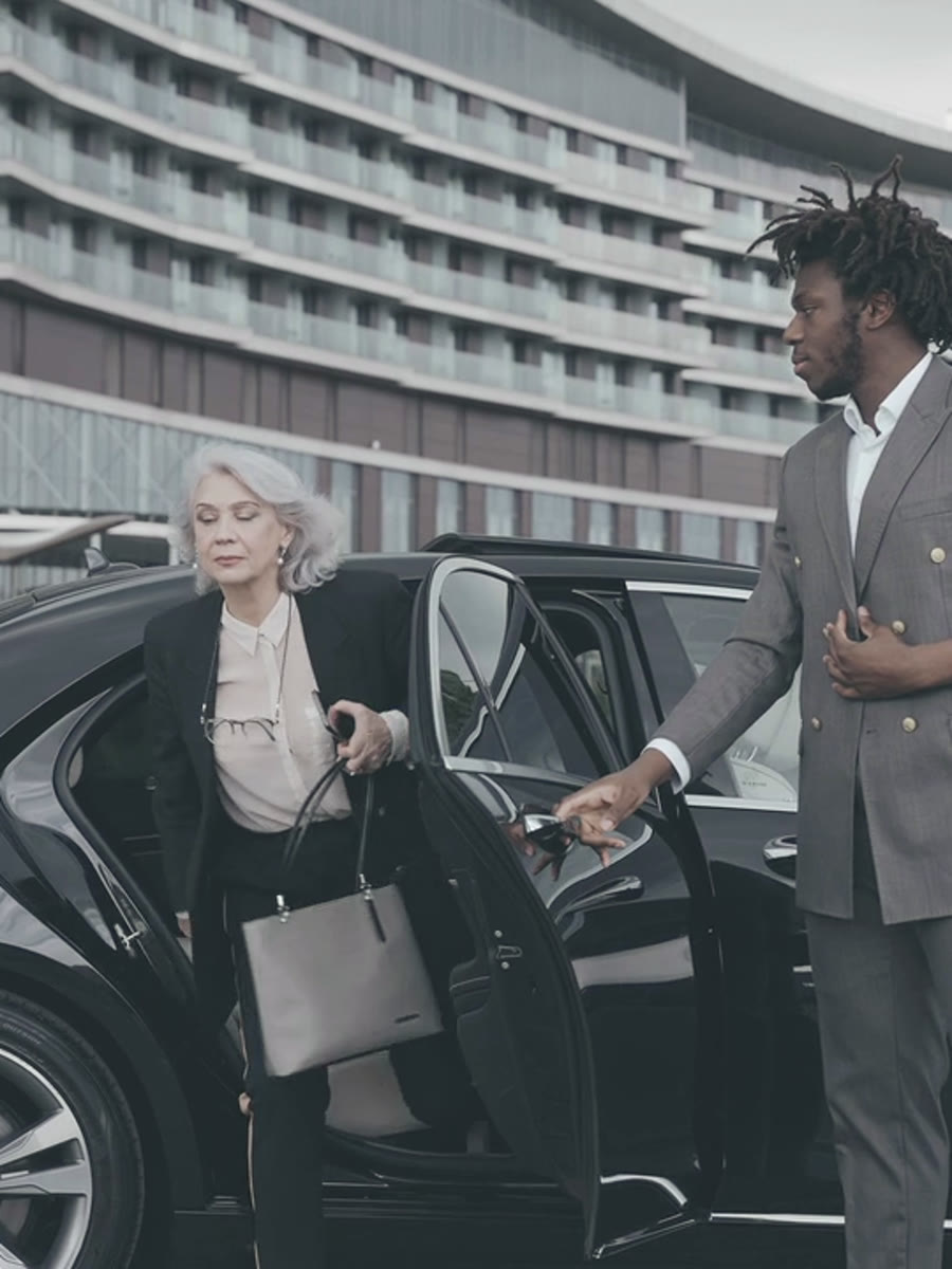 A DriveMe chauffeur holding the door for a client stepping out of a black saloon