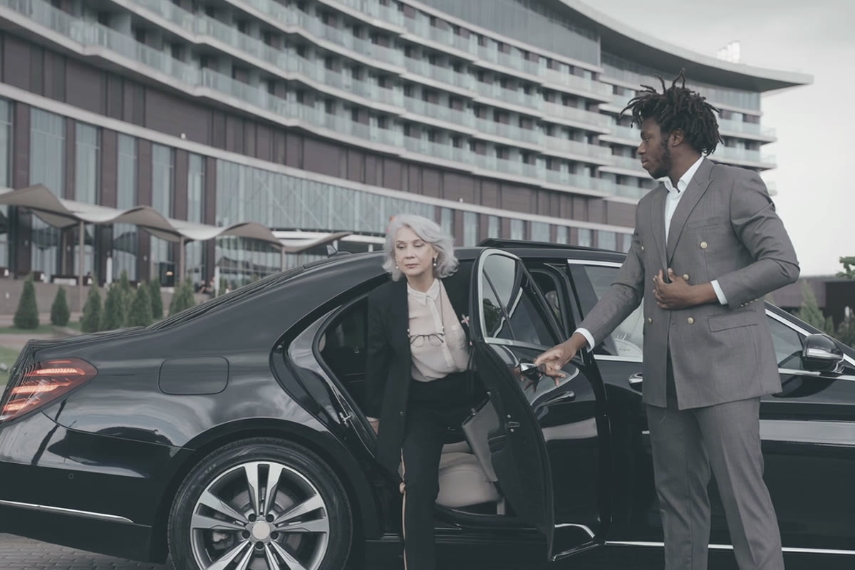 A suited chauffeur opening the rear door of a black saloon